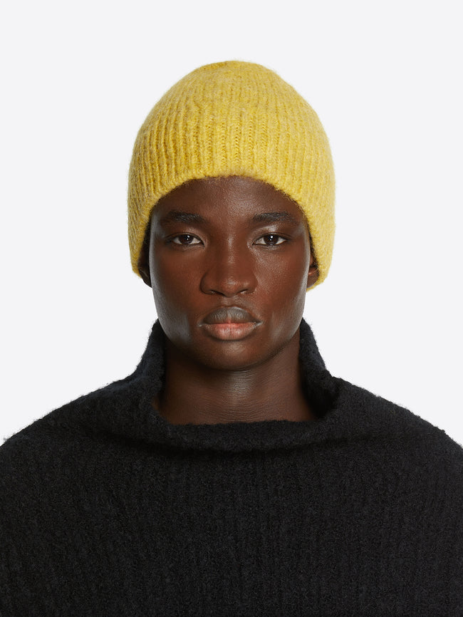 Model wearing a mustard colored wool beanie on a white background