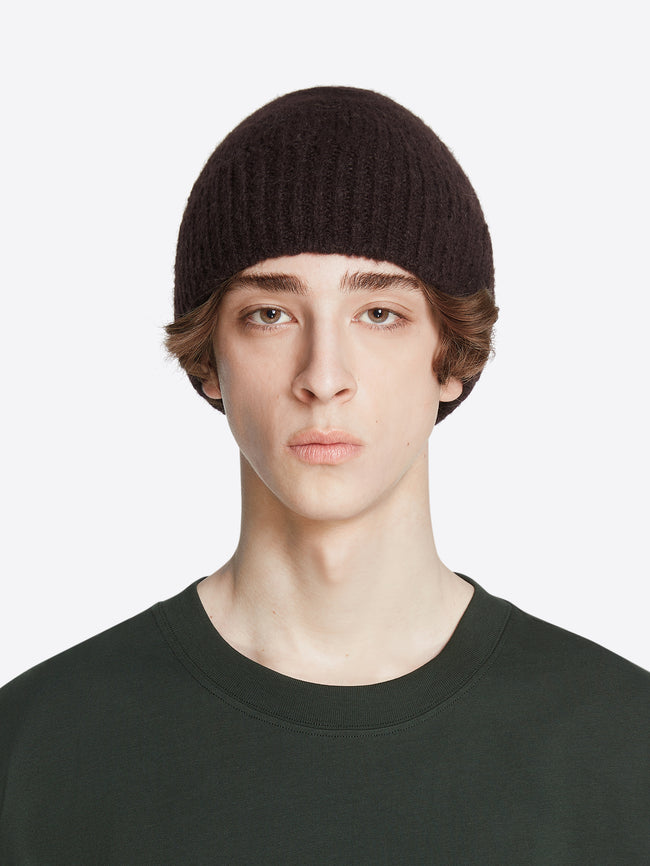 Model wearing a dark brown colored wool beanie on a white background