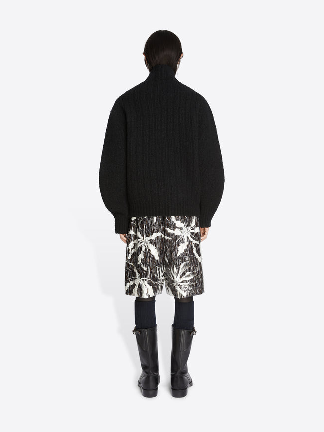 Backside of a model wearing a pair of black and white patterned shorts and a black oversized wool sweater on a white background