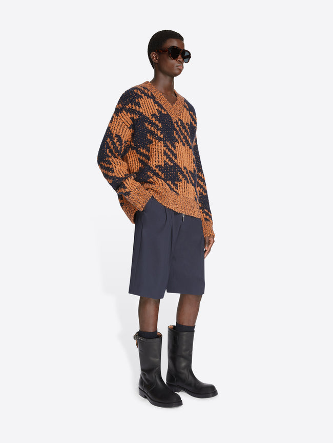 Model wearing navy shorts and a light rust and navy checkered graphic sweater on a white background