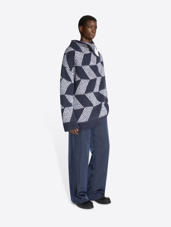 Model wearing a pair of light navy pants and a navy and white, oversized graphic sweater on a white background