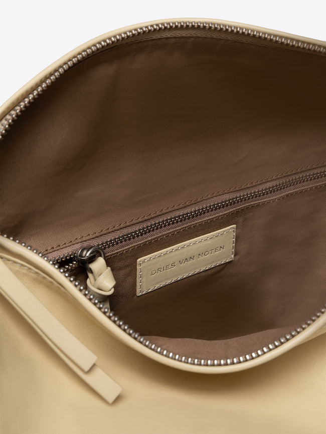 Close-up of a sand colored leather bag with a zipper, showing the Dries Van Noten label.