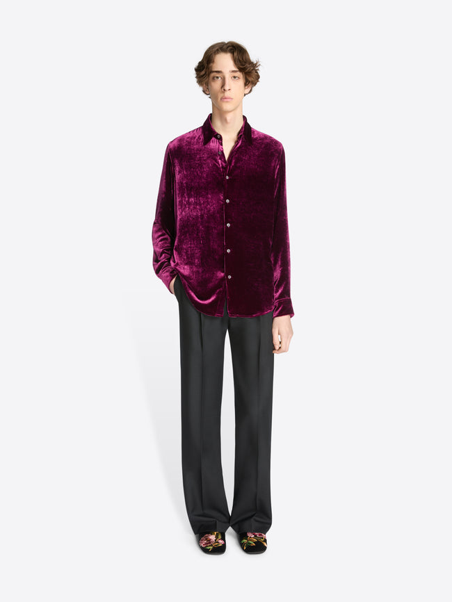 Person wearing a burgundy velvet shirt, black pants and black slippers with floral print on a white background