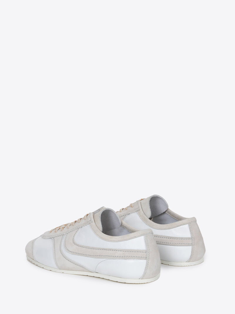 Backside of a pair of white suede sneakers with beige accents on a white background