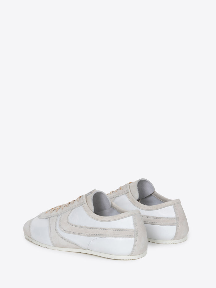 Backside of a pair of white suede sneakers with beige accents on a white background