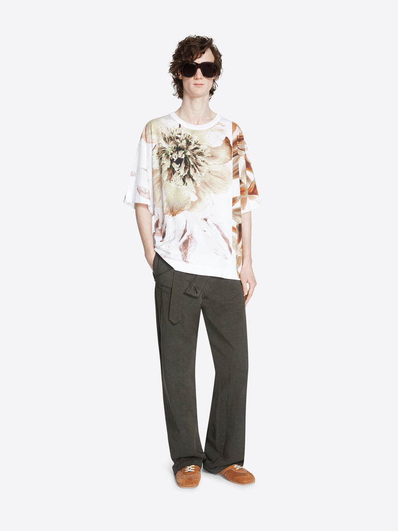 Person wearing a floral patterned shirt, gray pants and tan brown suede sneakers on a white background