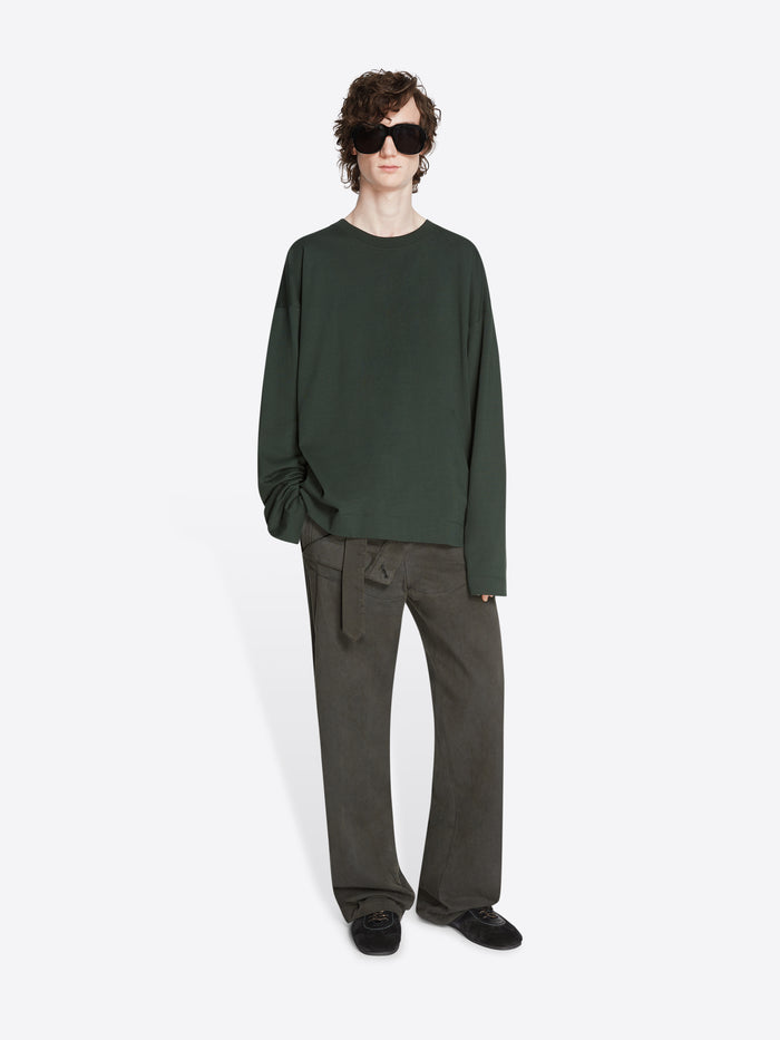 Person wearing a dark green long-sleeve shirt, gray pants and a pair of black suede sneakers on a white background