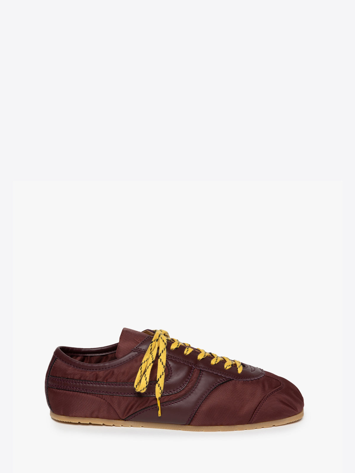 A low-top sneaker in dark burgundy fabric with yellow laces and a gum sole, shown from a side profile on a light gray background.