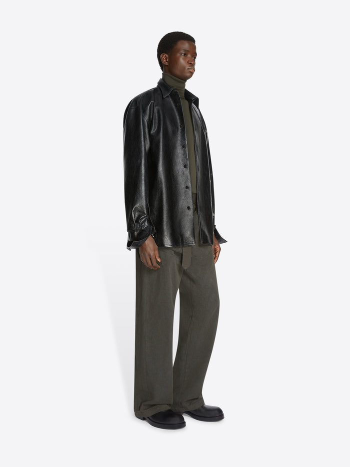Person wearing a black leather shirt and green pants on a white background