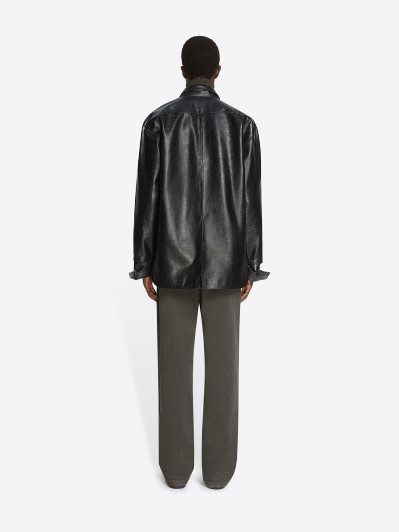 Person wearing a black leather shirt and green pants on a white background