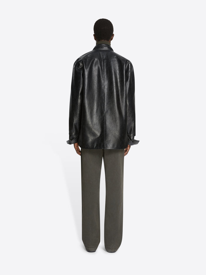 Person wearing a black leather shirt and green pants on a white background