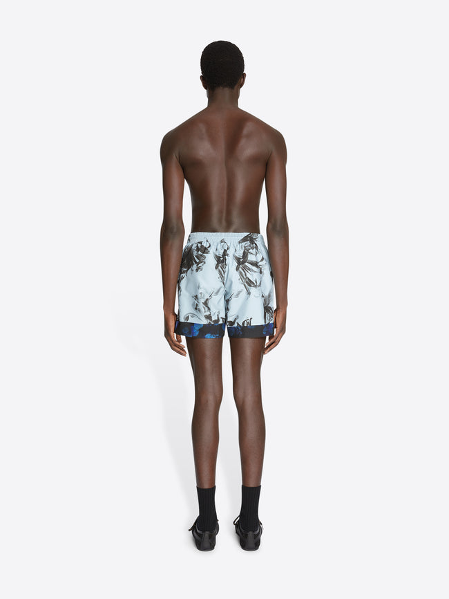 Backside of a model wearing mint colored, printed swim shorts on a white background