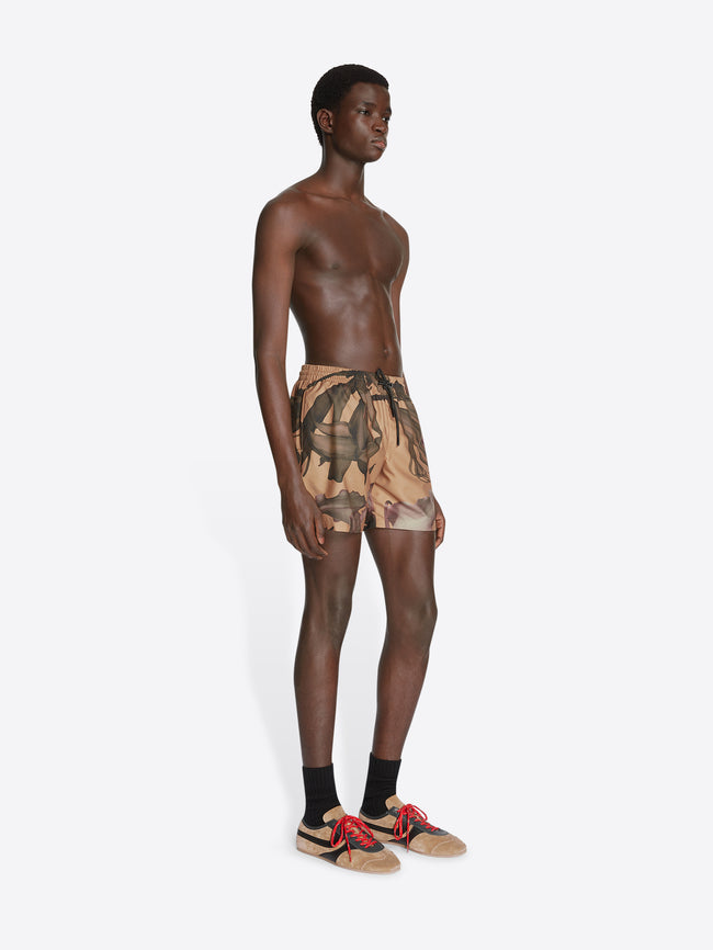 Model wearing ocra colored, floral printed swim shorts on a white background