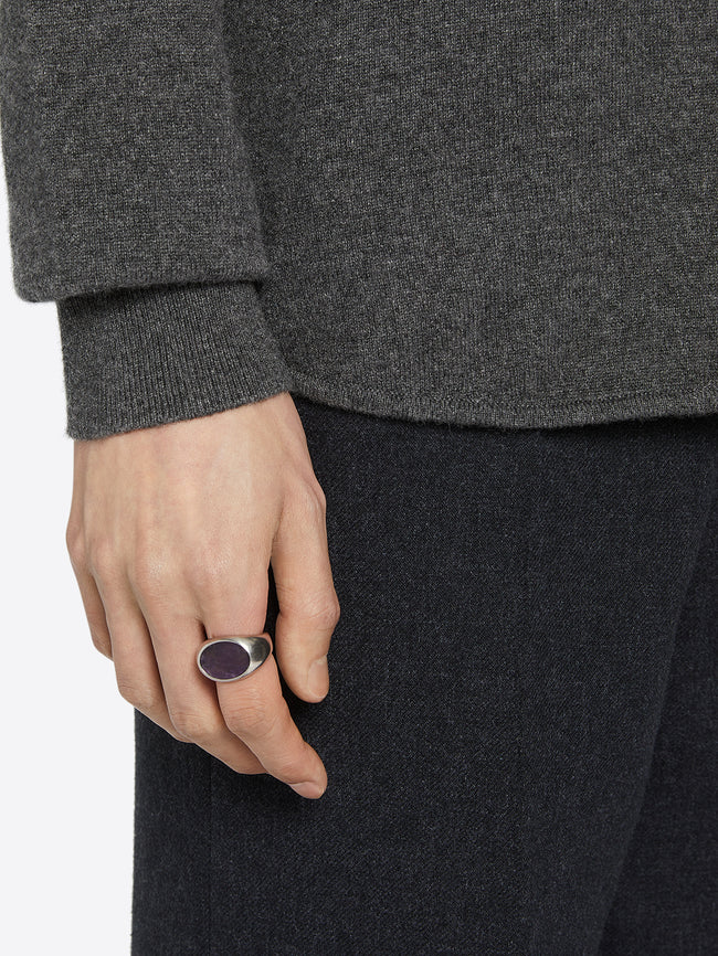 Person wearing a dark gray sweater and black pants with a silver ring with a flat dark purple stone on a white background