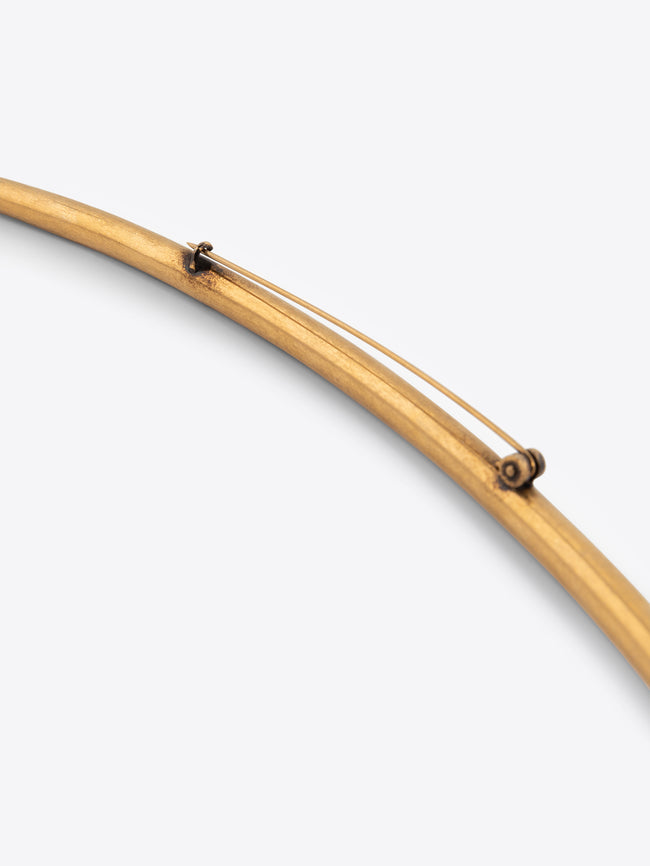 Long curved mat gold brooch on a white background