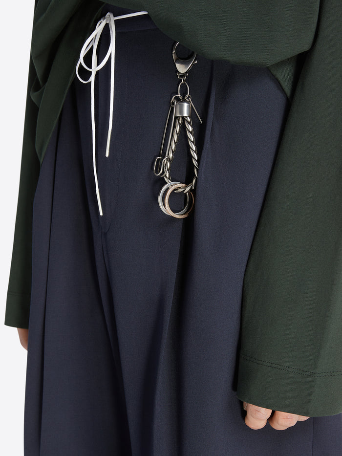 Palladium keychain with a safety pin and two rings being worn on a navy pair of trousers