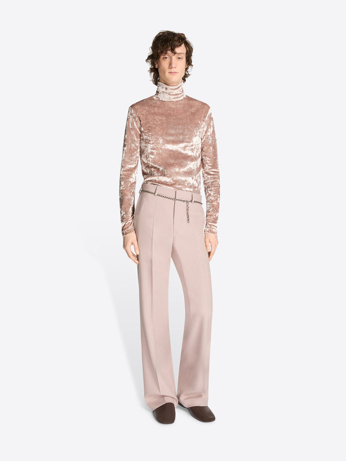 Person wearing a metallic top and beige pants wearing a metallic chain belt on a white background