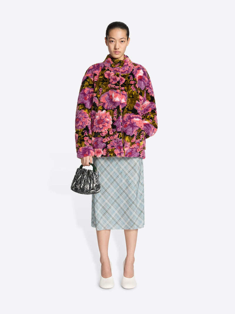 Woman wearing a floral jacket and plaid skirt with a handbag on a white background