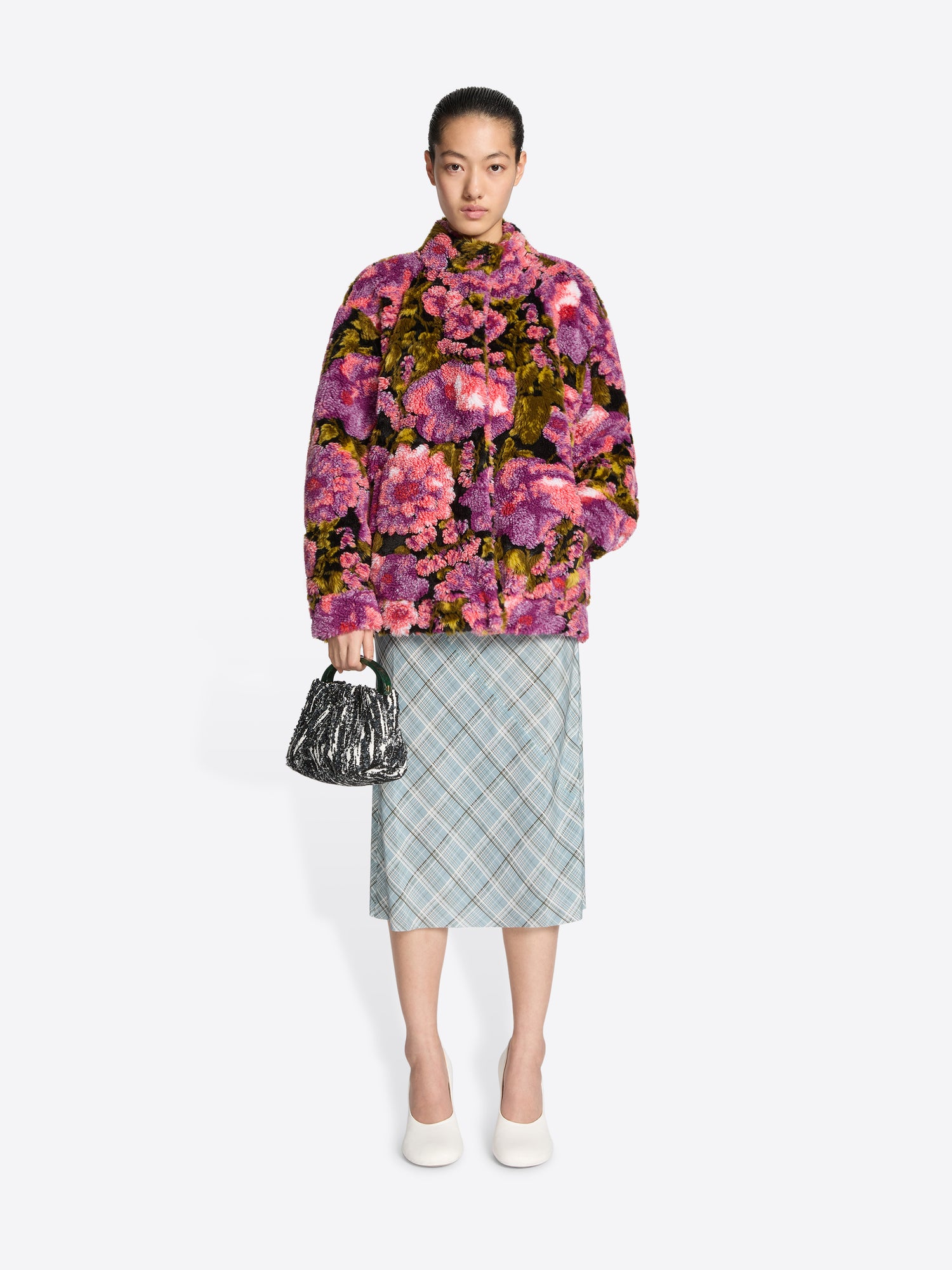 Woman wearing a floral jacket and plaid skirt with a handbag on a white background