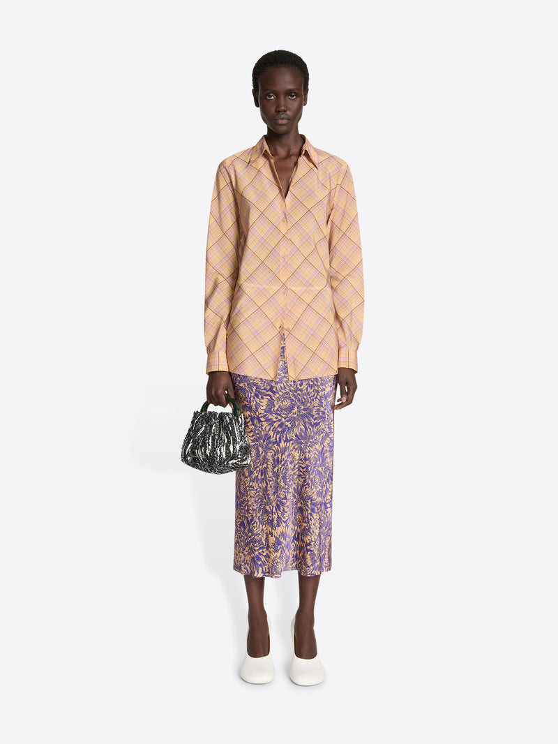 Woman wearing a patterned jacket and skirt with a handbag on a white background