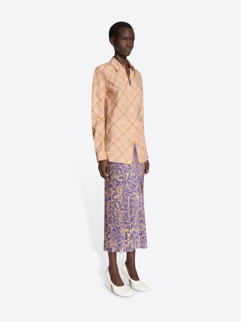 Model wearing a beige checkered jacket and purple floral skirt on a white background
