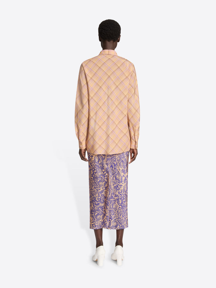 Person wearing a patterned beige jacket and purple skirt on a white background