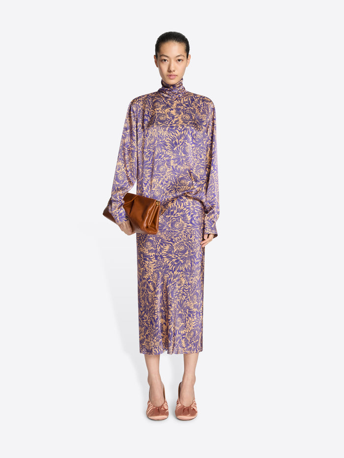 Woman wearing a purple floral dress holding a brown handbag on a white background