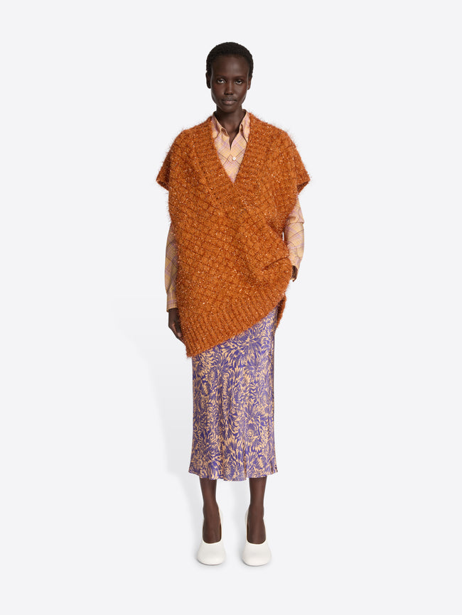 Woman wearing an orange knitted poncho over a patterned skirt on a white background