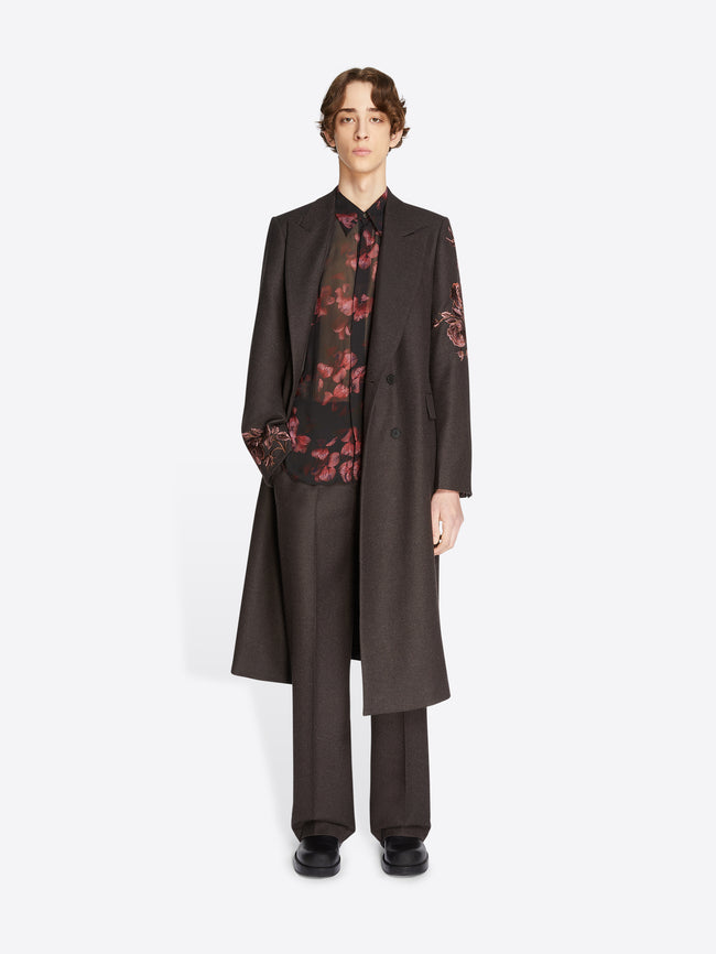 Person wearing a dark coat over a floral shirt on a white background