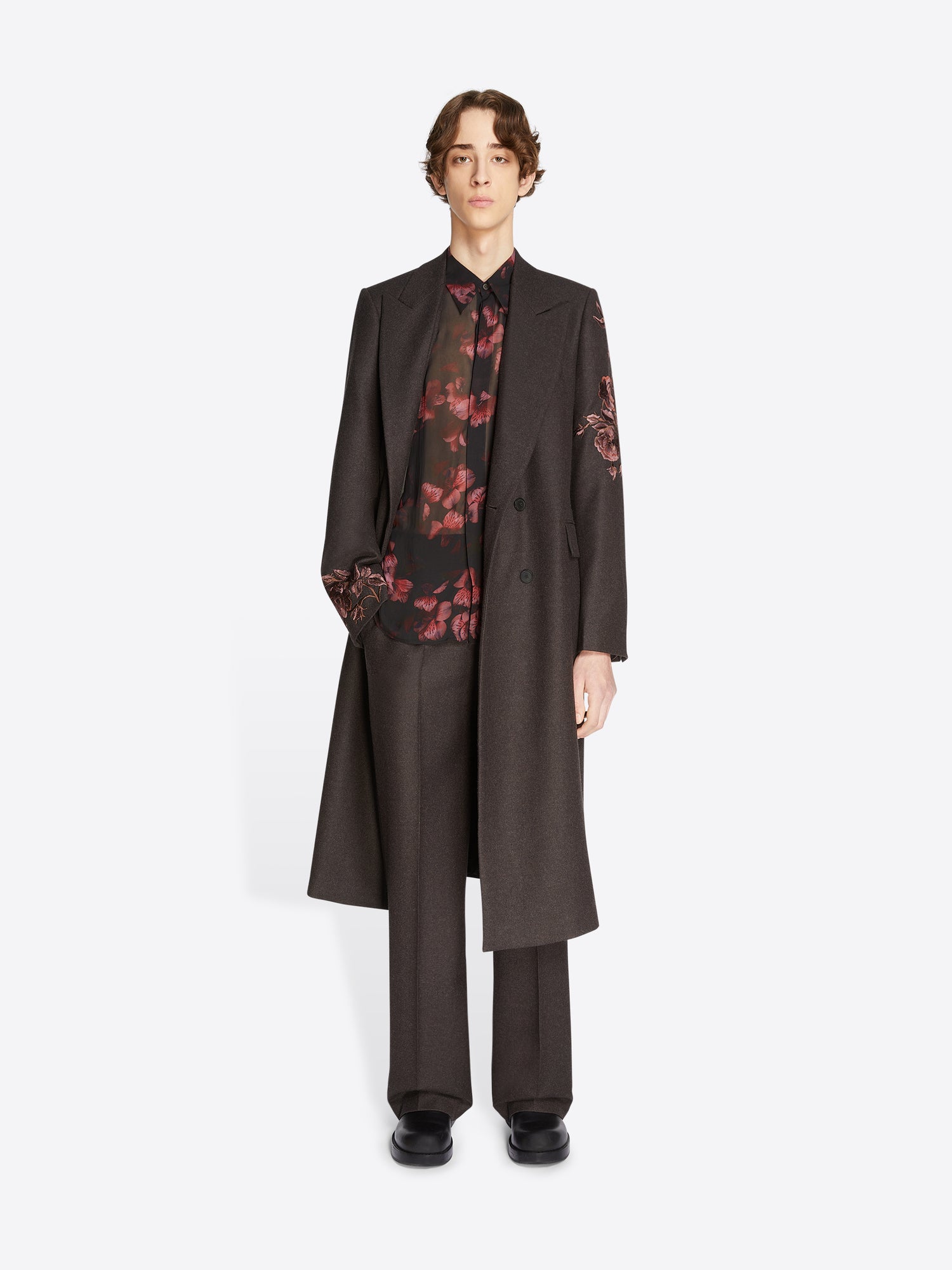Person wearing a dark coat over a floral shirt on a white background