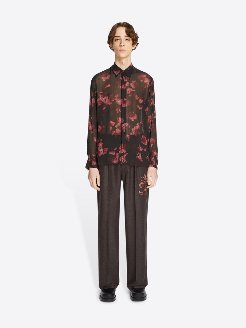 Person wearing a black floral shirt and dark pants on a white background
