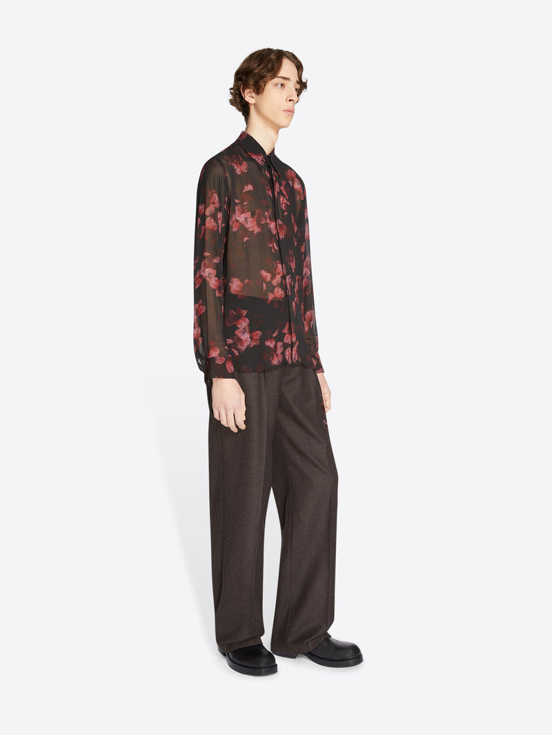 Person wearing a dark floral shirt and dark pants on a white background