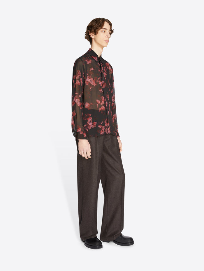 Person wearing a dark floral shirt and dark pants on a white background