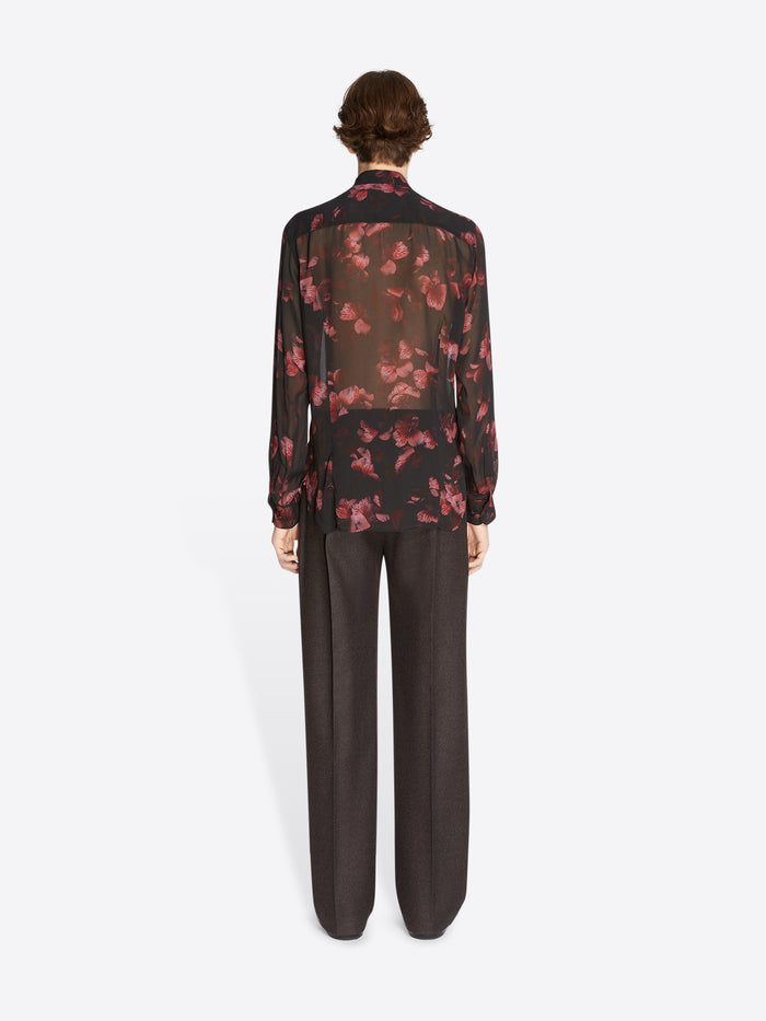 Person wearing a floral blouse and dark pants on a white background