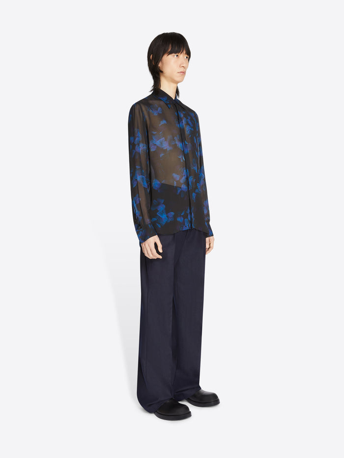 Person wearing a sheer black and blue floral shirt with wide-leg pants on a white background
