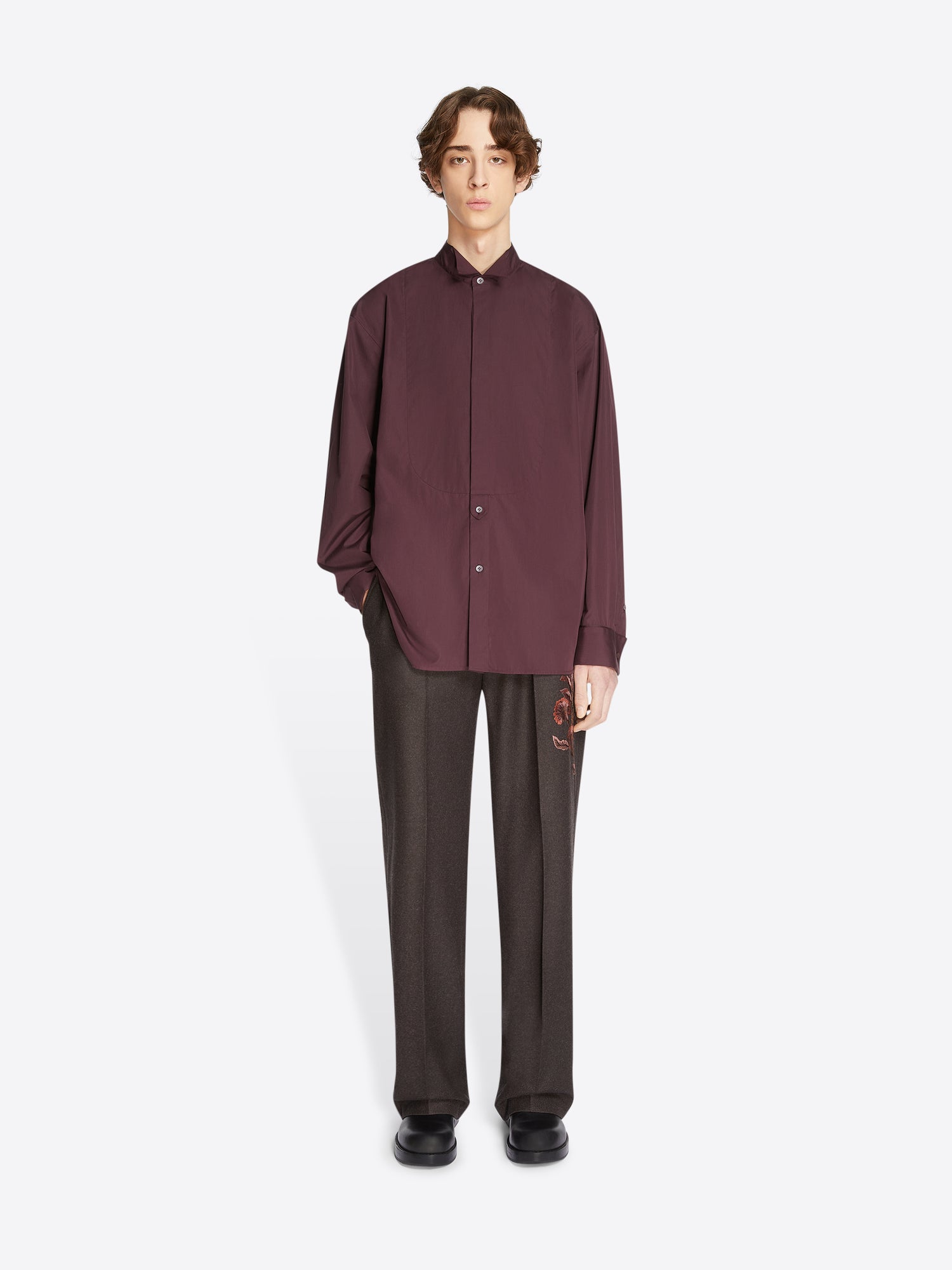 Person wearing a burgundy shirt and dark pants on a white background