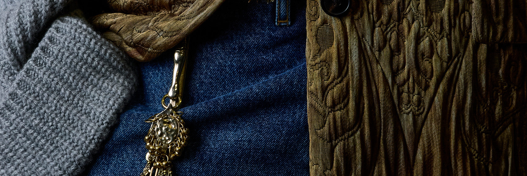 A close-up of a textured gold charm, hanging from a blue denim garment.