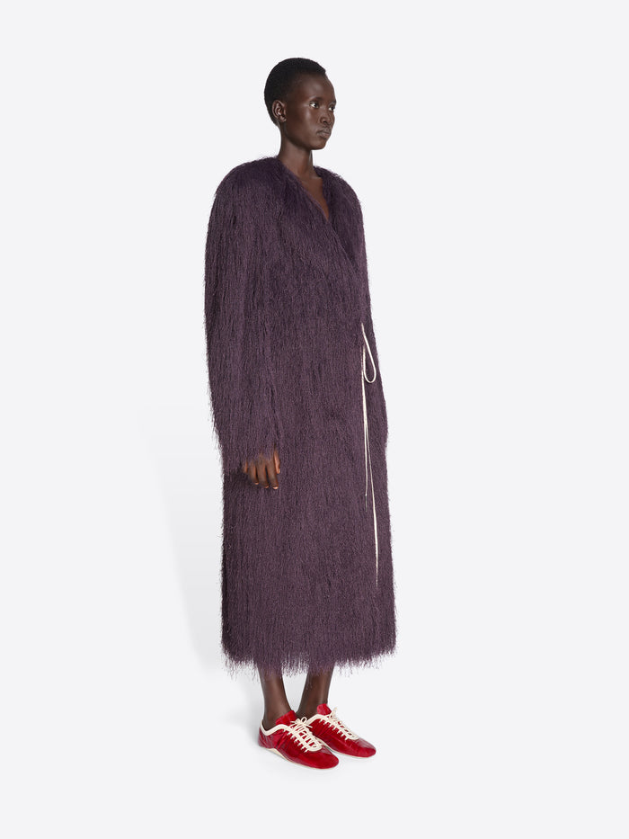 Person wearing a long dark purple coat and red sneakers on a white background - Dries Van Noten
