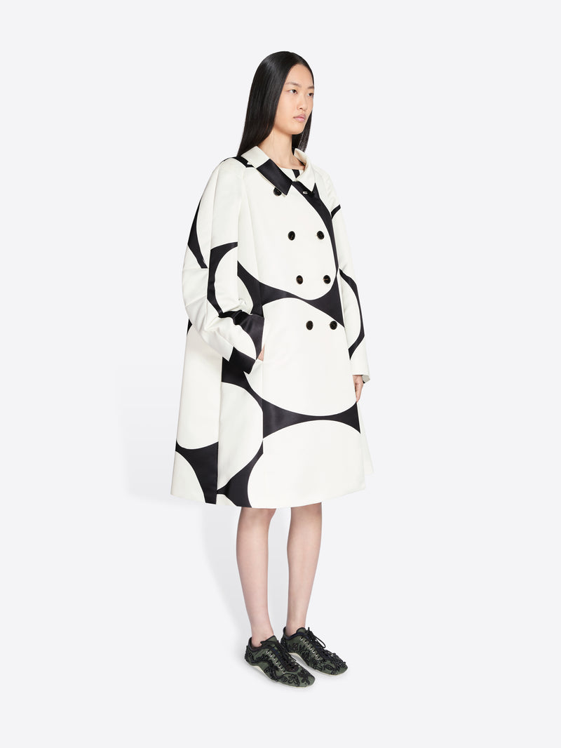 Person wearing a black and white patterned coat on a white background - Dries Van Noten