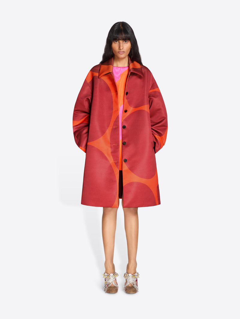 Person wearing a red and orange patterned coat on a white background - Dries Van Noten