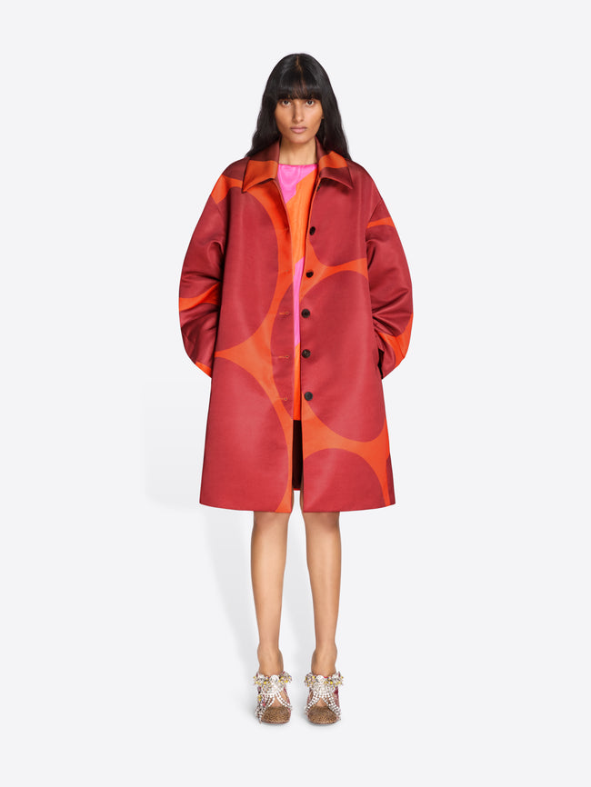 Person wearing a red and orange patterned coat on a white background - Dries Van Noten