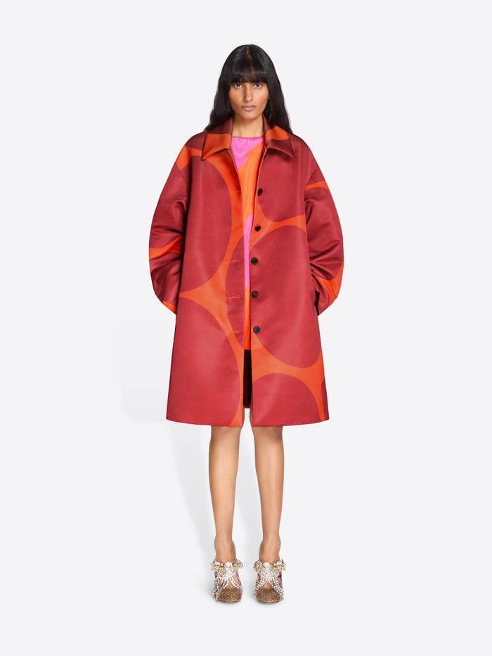 Person wearing a red and orange patterned coat on a white background - Dries Van Noten