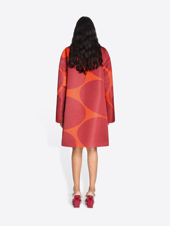 Person wearing a red and orange patterned coat on a white background - Dries Van Noten