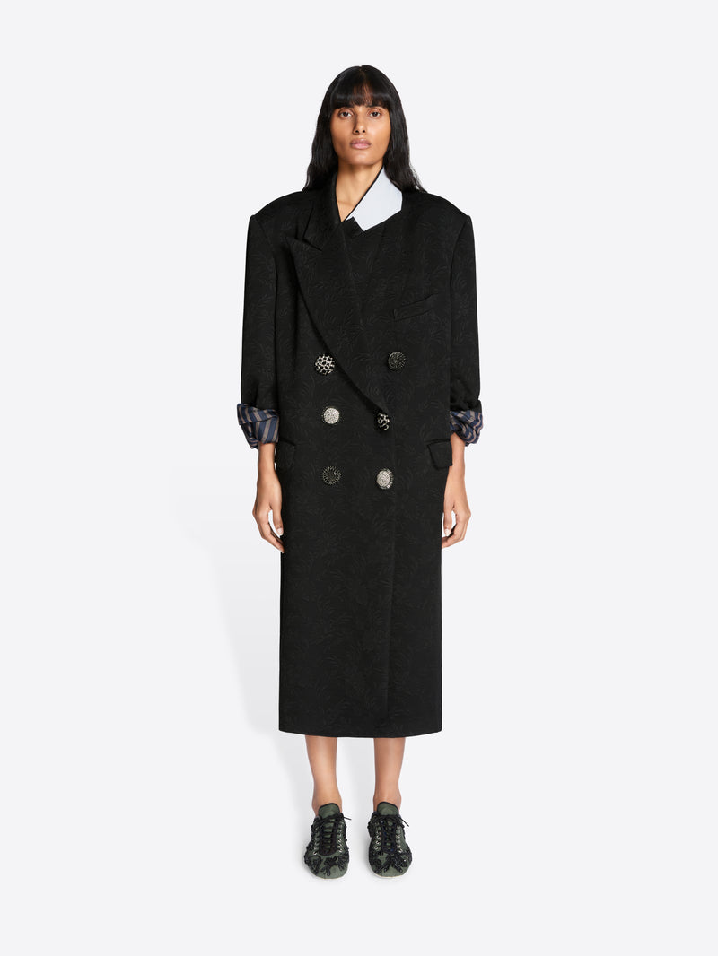 Person wearing a black coat with a white shirt underneath on a white background - Dries Van Noten