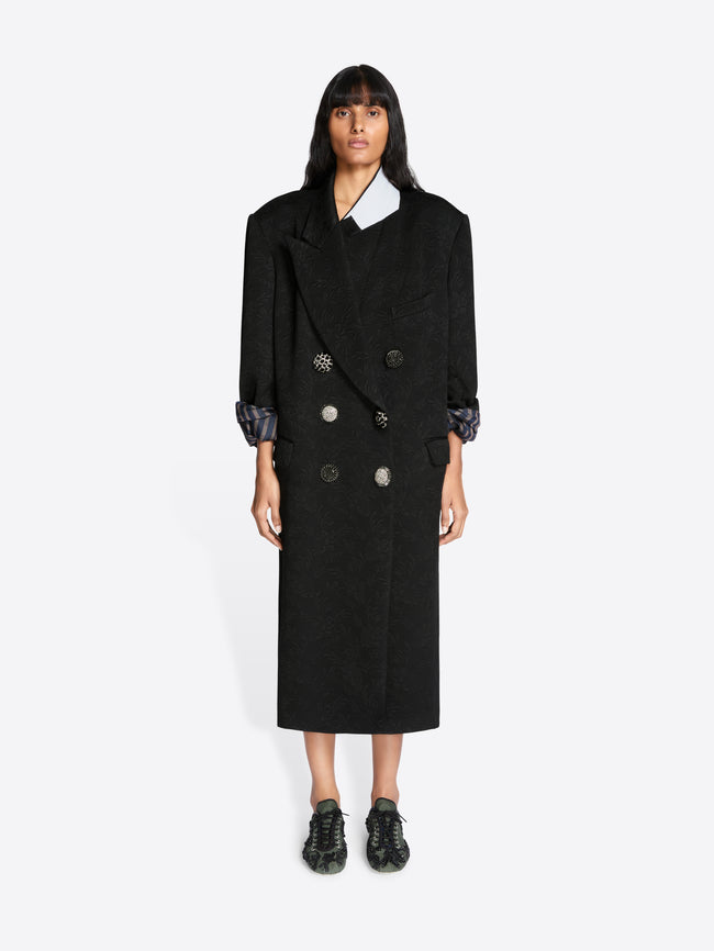 Person wearing a black coat with a white shirt underneath on a white background - Dries Van Noten