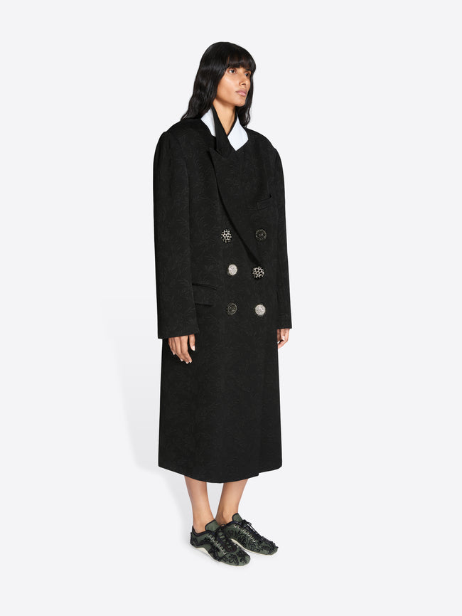 Person wearing a long black coat on a white background - Dries Van Noten