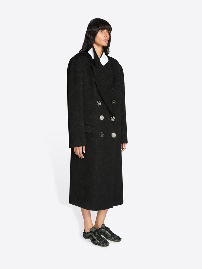 Person wearing a long black coat on a white background - Dries Van Noten