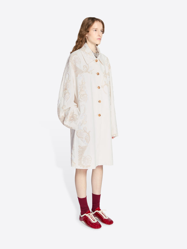 Person wearing a light-colored coat with a subtle pattern on a white background - Dries Van Noten