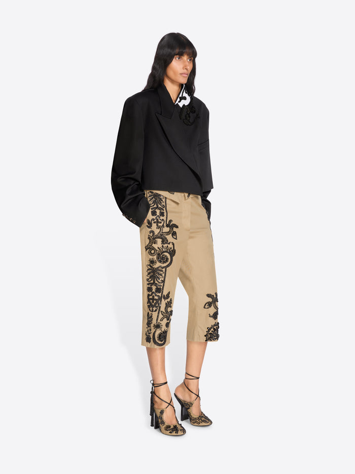 Woman wearing a black blazer and beige pants with black floral embroidery on a white background - Dries Van Noten