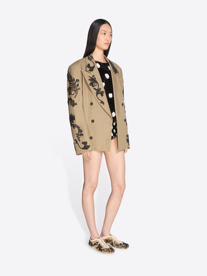 Woman wearing a beige blazer with black floral embroidery on a white background - Dries Van Noten